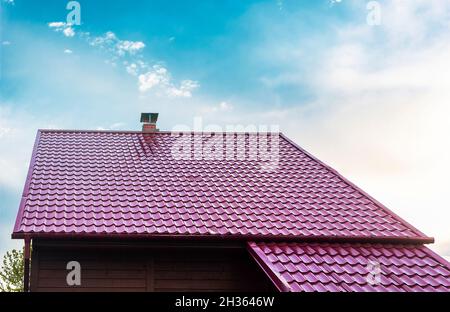 Dach eines Hauses mit einem roten Ziegeldach unter einem klaren blauen Himmel im Sommer. Stockfoto