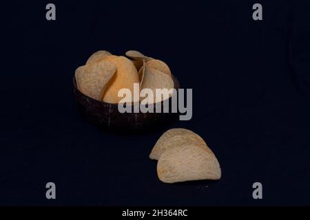 Kartoffelchips in einer Tasse und außen auf schwarzem Hintergrund Stockfoto