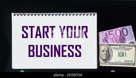 Text STARTEN SIE IHR MOTIVATIONSANGEBOT AUF Notizblock und schwarzem Hintergrund mit Euro und Dollar Stockfoto