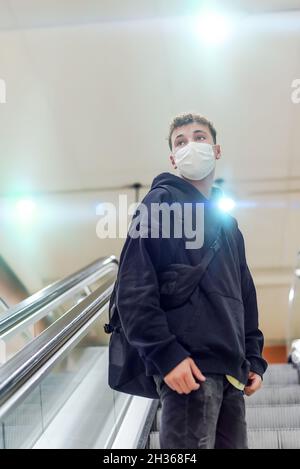 Ein junger Mann mit Rucksack und weißer Maske klettert in einer U-Bahnstation auf eine Rolltreppe Stockfoto