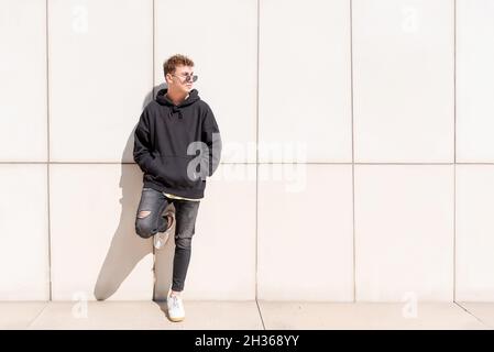 Junger Mann im schwarzen Sweatshirt posiert mit seiner Sonnenbrille im Freien Stockfoto