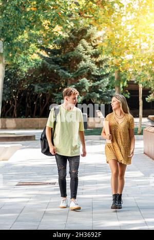 Zwei junge Studenten, ein Mann und eine Frau, gehen auf dem Campus umher und sprechen über ihr Studium Stockfoto