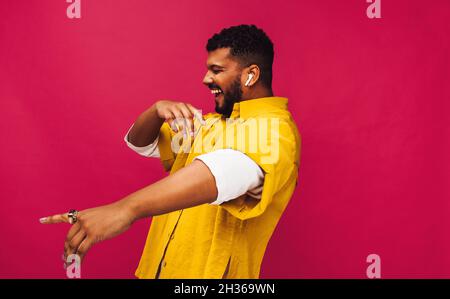 Lächelnder junger Mann, der zu seiner Lieblingsmusik in einem Studio tanzt. Fröhlicher junger Mann, der Musik mit kabellosen Ohrhörern streamt. Sorgloser junger Mann sta Stockfoto
