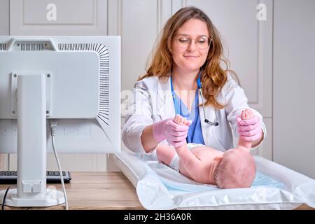 Der Arzt macht Gymnastik und massiert ein neugeborenes Baby. Krankenschwester in Uniform, die dem Kind Aufwärmübungen macht Stockfoto