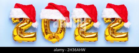 Goldene Folienballons im weihnachtsmannhut in Form von Zahlen 2022 auf blauem Hintergrund. Frohes neues Jahr. Banner in der Draufsicht. Stockfoto