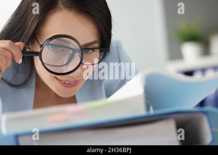 Frau, die Dokumente in einem Ordner durch eine Lupe betrachtet Stockfoto