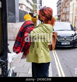 Anonyme junge Frau mit leuchtend roten Haaren stehend und mit Mobiltelefon ein Foto in Einer Londoner Straße zu machen Stockfoto