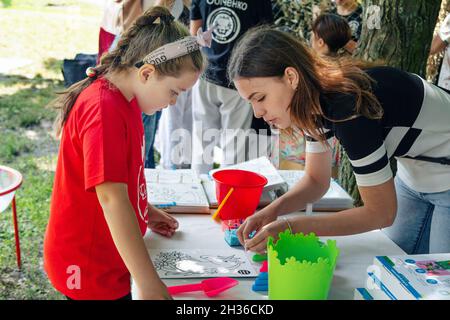 Zaporizhia, Ukraine- 19. Juni 2021: Charity Familienfest: Frau – Freiwillige erklärt einem Mädchen, wie man das Bild bei Kunst und Handwerk im Freien malen kann Stockfoto