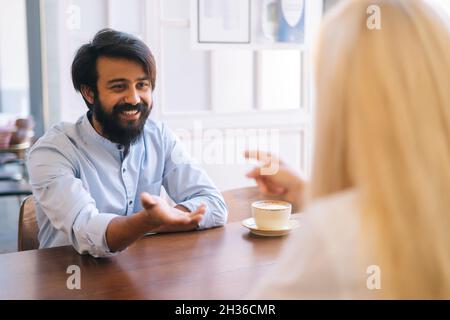 Nahaufnahme von hinten von einer nicht erkennbaren blonden jungen Frau, die mit einem fröhlichen bärtigen jungen Geschäftsmann handshaking, der den Deal abschließt. Stockfoto