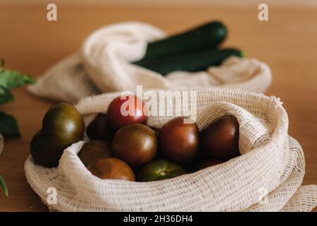 Tomate in Leinwand Lebensmittelbeutel. Gemüse in wiederverwendbaren Öko-Baumwollbeuteln auf Holztisch. Zero Waste Shopping-Konzept. Kunststoffartikel Stockfoto
