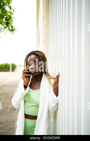 Vertikales Porträt einer Afro-Frau mit Zöpfen, die mit dem Handy sprechen und der Kamera im Freien gegenüberstehen Stockfoto
