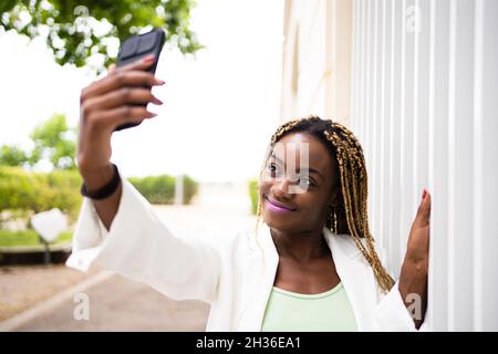 Portarit einer lächelnden jungen afrikanischen Frau, die im Freien Selfie mit einem Handy macht Stockfoto