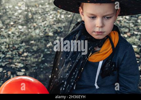 Halloween Kinder. Niedlicher kleiner Junge traurig an Halloween, Kind im Hexenhut mit orangefarbenem Jack O Laterne Ballon. Stockfoto