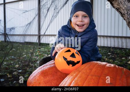 Halloween Kinder. Niedlicher kleiner Junge, Kind mit einem orangefarbenen Eimer mit Jack O Lantern Süßigkeiten, in der Nähe des Kürbisses und Spinnweben. Frohe Halloween. Stockfoto