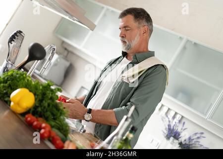 Schöner älterer Mann, der zu Hause kocht und in der Küche Salat zubereitet Stockfoto
