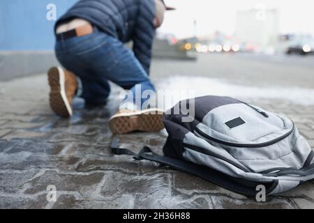 Rucksack liegt auf rutschigen Pflasterplatten in der Nähe eines herunterfallenden Mannes in der Nähe Stockfoto