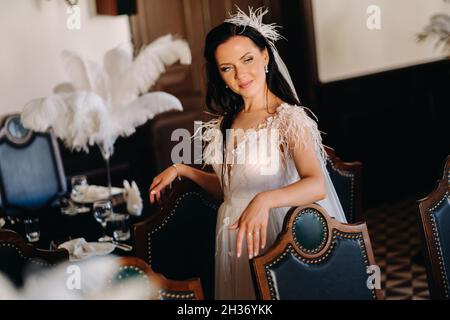 Eine stilvolle Braut in einem Hochzeitskleid im Inneren eines Restaurants, das mit Federn auf den Tischen dekoriert ist. Stockfoto