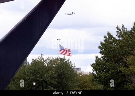Eine amerikanische Flagge und ein Flugzeug, das durch die Unisphere im Flushing Meadows Corona Park in Queens, New York City, gesehen wird. Stockfoto