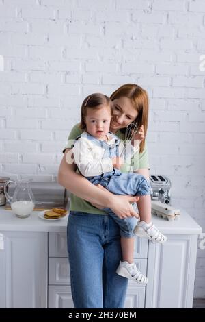 Glückliche Mutter hält Tochter mit Down-Syndrom und Schneebesen in der Küche Stockfoto