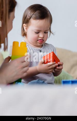 Kleinkind Mädchen mit Down-Syndrom hält Baustein in der Nähe der Mutter zu Hause Stockfoto