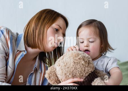 Mutter im Gespräch mit Kleinkind Tochter mit Down-Syndrom hält weiches Spielzeug zu Hause Stockfoto