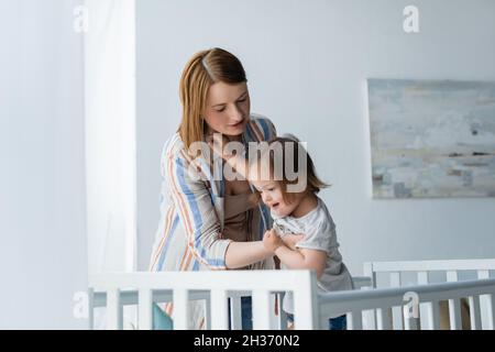 Mutter hält das Baby mit Down-Syndrom in der Nähe der Krippe zu Hause Stockfoto