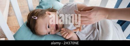 Mutter hält Hand eines positiven Kindes mit Down-Syndrom in der Krippe, Banner Stockfoto