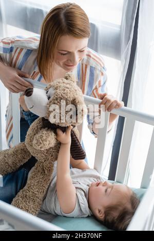 Mutter schaut auf das Baby mit Down-Syndrom und hält ein weiches Spielzeug in der Krippe Stockfoto