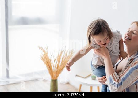 Mutter hält lächelnde Tochter mit Down-Syndrom zu Hause Stockfoto