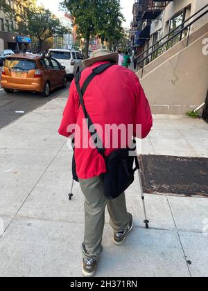 Die alte Person schlurft mit Hilfe von Wanderstöcken auf der 7th Avenue in Brooklyn, New York. Stockfoto