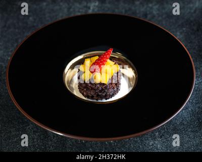 Schwarzer klebriger klebriger Reis mit Mango- und Kokoscreme in schwarzer Schale auf dunkelgrauer Steinoberfläche Stockfoto