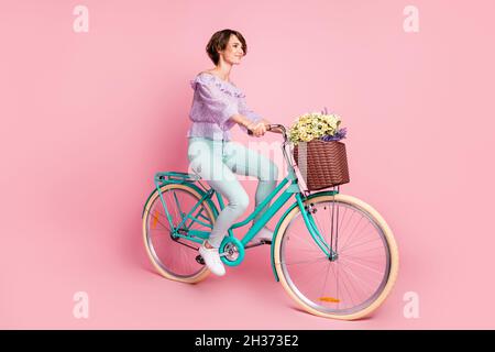 Full size Profil Seitenfoto der jungen schönen ziemlich verträumt Mädchen Fahrrad mit Blumen im Korb isoliert auf rosa Hintergrund reiten Stockfoto