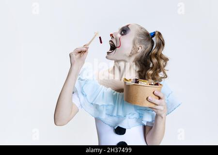 Nahaufnahme mystisch blonde Mädchen in halloween Make-up und gruselige Gesichtsausdruck essen Gelee Süßigkeiten isoliert auf grauem Hintergrund Stockfoto