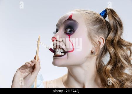 Nahaufnahme mystisch blonde Mädchen in halloween Make-up und gruselige Gesichtsausdruck essen Gelee Süßigkeiten isoliert auf grauem Hintergrund Stockfoto