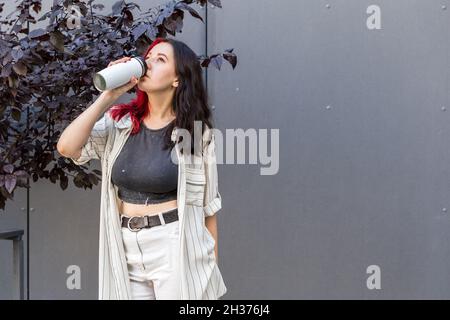 Junge Frau trinkt aus dem wiederverwendbaren Isolierbecher. Bleib hydratisiert Stockfoto