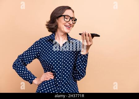 Foto des optimistischen Manager gealterte Dame Telefon tragen Brillen blaues Hemd isoliert auf beigefarbenem Hintergrund sprechen Stockfoto