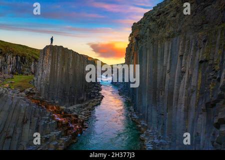 Wanderer, der bei Sonnenuntergang auf dem Gipfel des Studlagil Canyon in Island steht Stockfoto