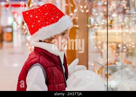 Boys in Santas Hut schaut durch das Fenster auf dem Markt in den Laden. Platz zum Kopieren, Platz für Text, Banner Stockfoto