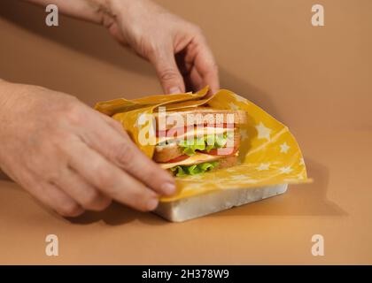 Ein traditionelles Sandwich aus getoasteten Brotscheiben, Käse, Schinken und frischem Salat, eingewickelt in wiederverwendbares Bienenwachspapier aus biologischem Anbau. Wir Feiern National Sandwi Stockfoto