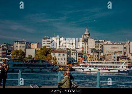 Eminonu,Istanbul,Türkei-Oktober-Samstag-2021: Zwei alte Leute sitzen unter der Sonne. Blick auf den Galata-Turm und die Fähre Stockfoto