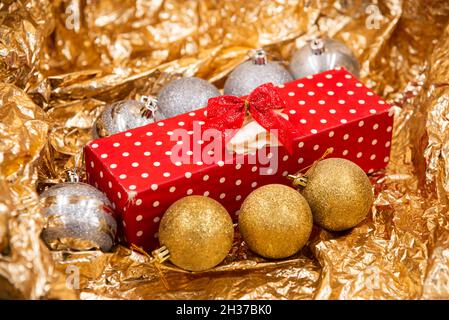Weihnachten dekoriertes Geschenk mit roten und weißen Punkten auf Papier mit roten Quasten und Weihnachtsbaumkugeln Dekorationen isoliert auf einem glänzenden orangen Hintergrund Stockfoto