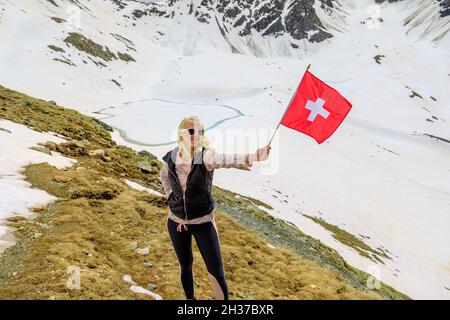 Tourist Frau mit schweizer Flagge im Schnee auf dem Muottas Muragl Berg der Schweiz. Beliebte Bergausflüge am Lej Muragl in Graubünden Stockfoto