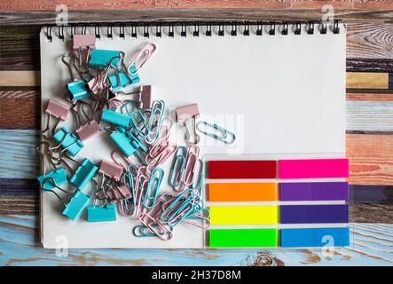 Sammlung von verschiedenen Arten von Büroklammern auf einem weißen Notizblock und bunten Stickern. Ort zum Schreiben Stockfoto