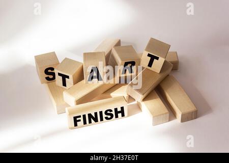 Die Wörter Start und Finish sind auf Holzblöcken und einem weißen Hintergrund geschrieben. Stockfoto