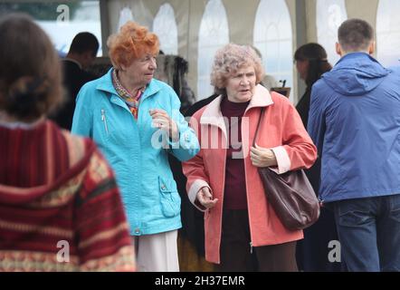 Zwei ältere Freundinnen in herbstlichen Outfits lächeln sich gegenseitig auf einem Pfad mit Pflanzen und Bäumen an. 3. September 2016, Minsk Stockfoto