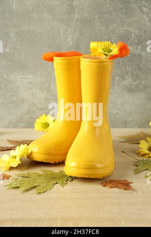 Gummistiefel mit Blumen auf Holztisch mit Blättern. Stockfoto