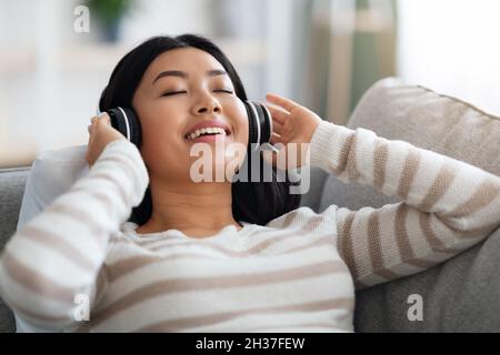 Lieblingsbeschäftigung. Schöne Koreanische Frau Trägt Kabellose Kopfhörer Musik Zu Hause Hören Stockfoto