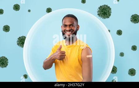 Fröhlicher afroamerikanischer junger Mann zeigt Schulter mit Gips nach der Impfung und Daumen hoch Stockfoto