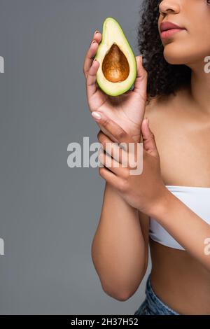 Teilansicht der afroamerikanischen Frau mit perfekter Haut halten Schnitt Avocado isoliert auf grau Stockfoto