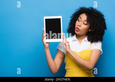 Erstaunt afroamerikanische Frau hält digitale Tablette mit leerem Bildschirm auf blau Stockfoto